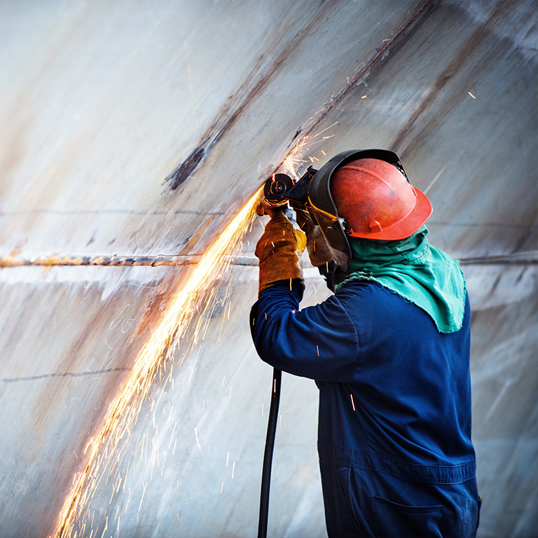 Worker grinding a boat hull, producing bright sparks while wearing helmet, gloves and protective gear — image representing third party liability boat insurance